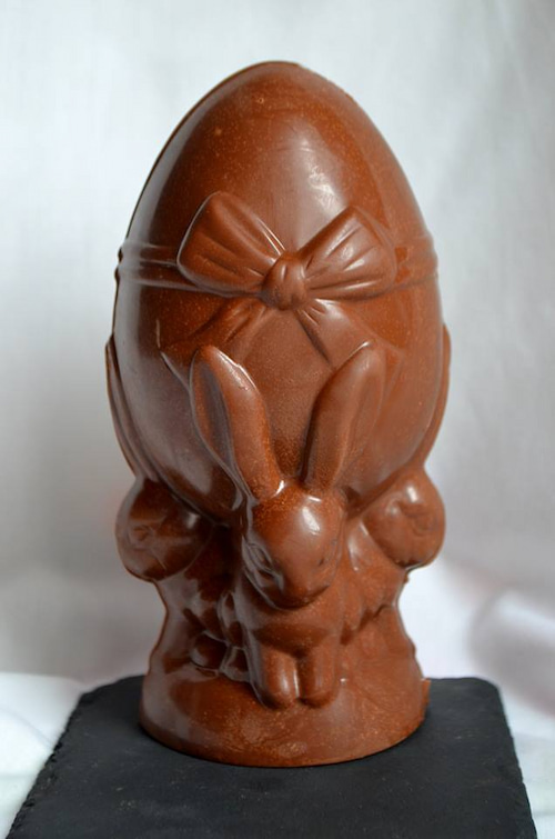 Oeuf de pâques lapin en chocolat au lait, posée sur ardoise et sous fond blanc