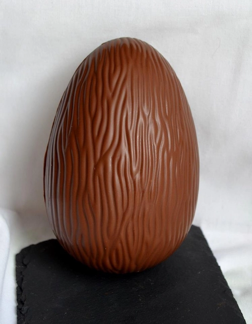 Oeuf de pâques en chocolat stayer au chocolat au lait, posée sur ardoise et sous fond blanc